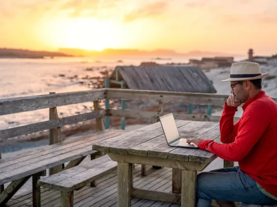 digital nomad sitting outdoors on the beach with a laptop alone doing telecommuting at sunset